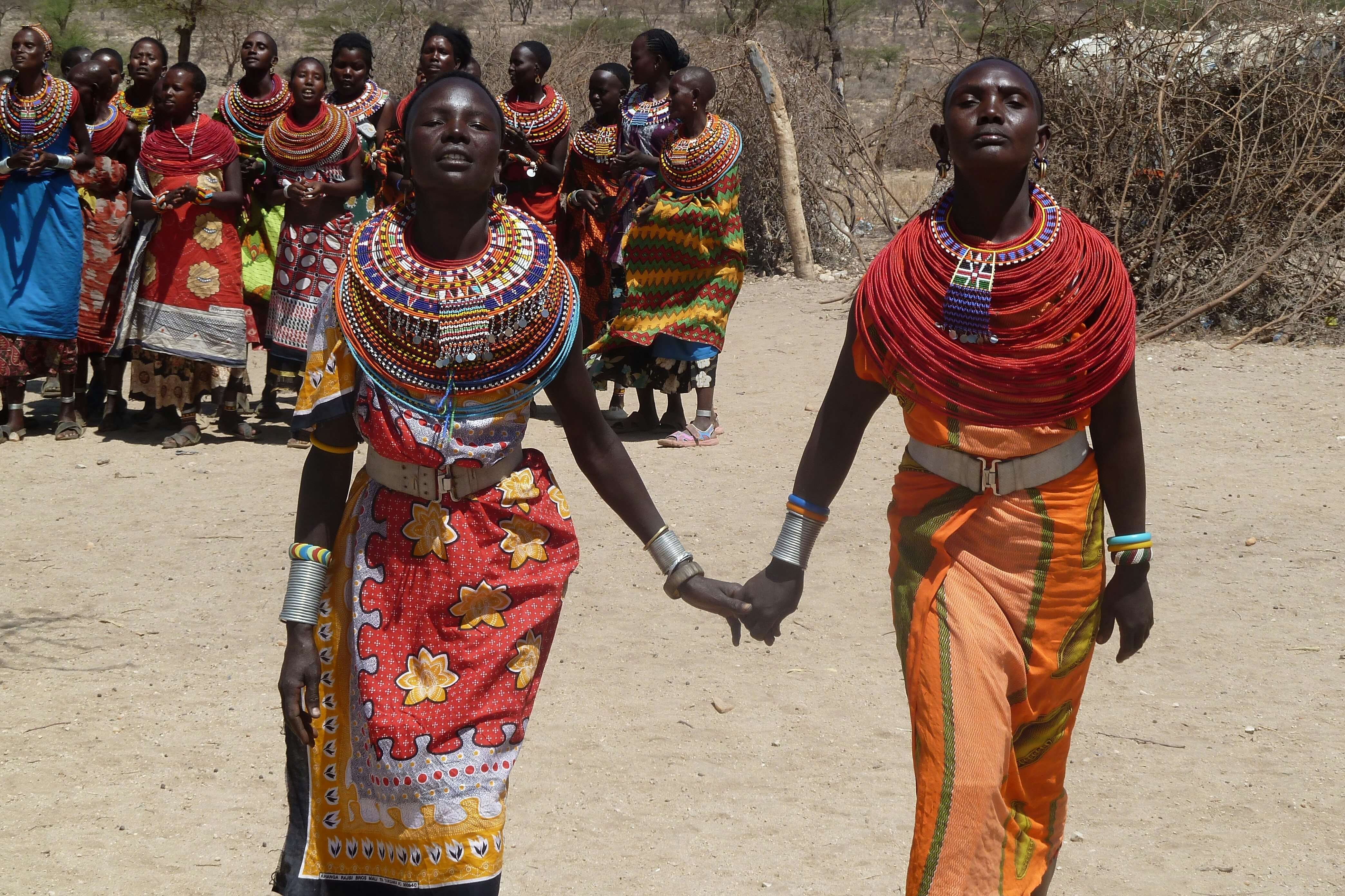 Two African women holding hands in traditional tribal outfits